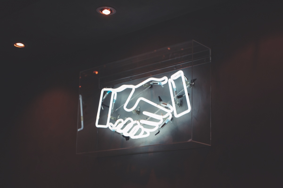 Neon sign of a handshake in a dark room.