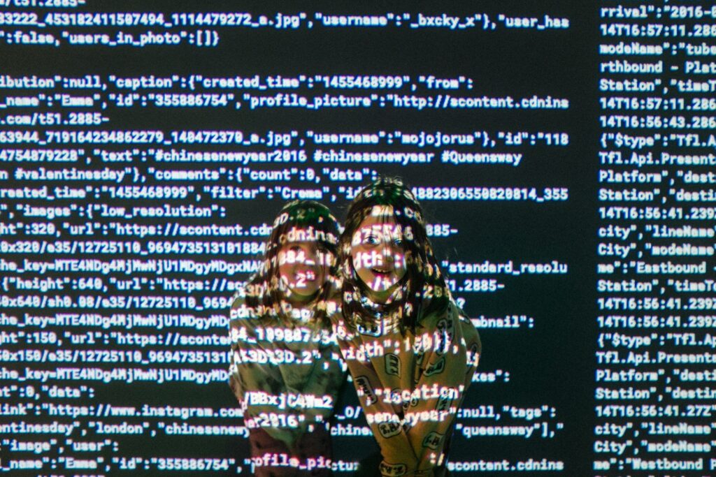 Two young girls peering out from a screen full of computer code.