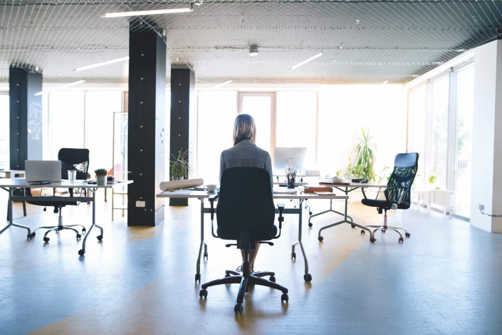 Woman manager working alone in open plan office, daytime, surrounded by empty desks.