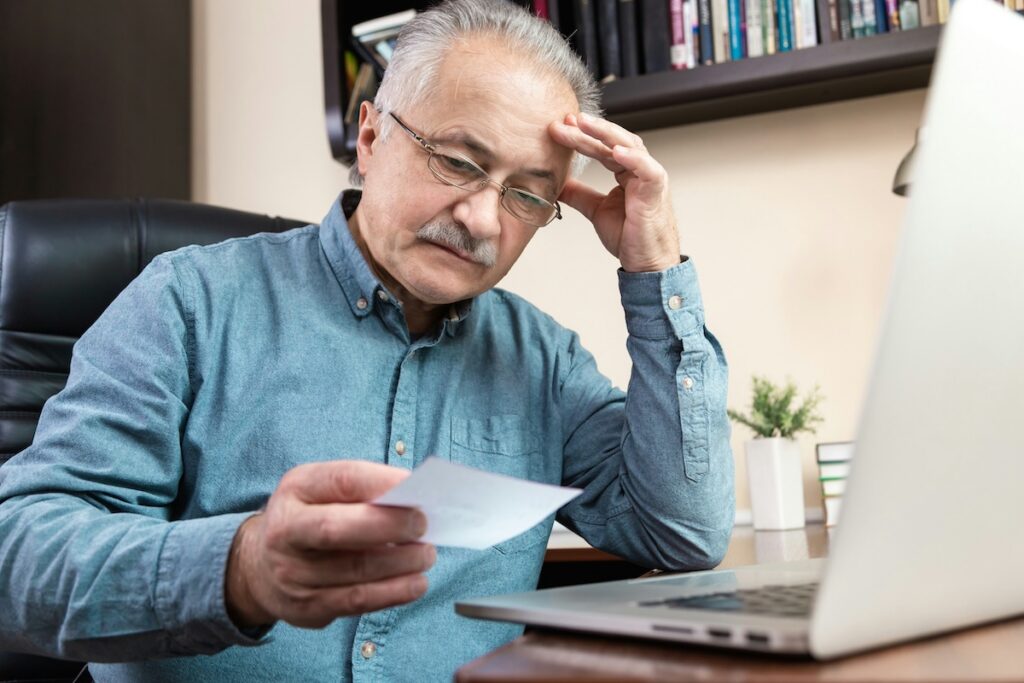 Older man looking worried working on laptop