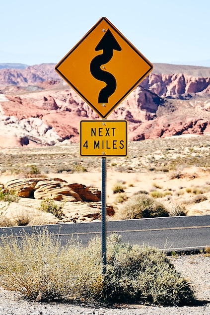 Sign in desert indicating dangerous bends for the next 4 miles